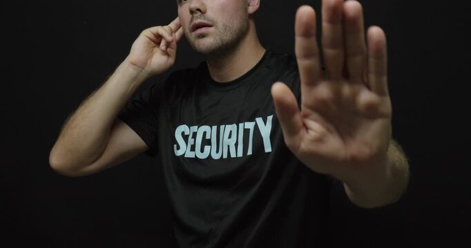 Security guard making a stop gesture with his hand while communicating through an earpiece. Concept for access control, protection, restricted entry and security enforcement.