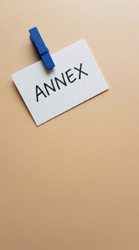 Annex label on white card with blue clip on beige background. Business document attachment concept, additional information, appendix.