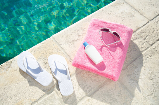 Flip flops, towel, sunglasses, and sunscreen by pool edge