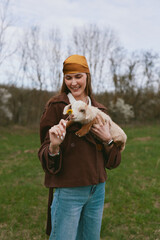 Naklejka premium A smiling woman outdoors gently offers a yellow flower to a playful goat kid, capturing a warm lifestyle moment in a rural field bathed in natural light and calm atmosphere.