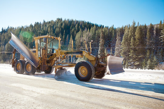 Motor grader plowing snow on a sunny winter mountain road