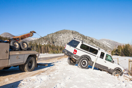 A tow truck pulls a midsize truck out of a snow filled ditch