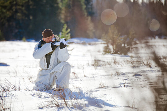 A hunter wearing  a coldweather camouflage outfit aims a rifel while