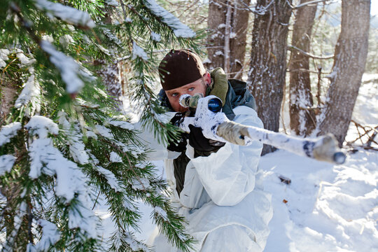 Soldier in winter camouflage aiming sniper rifle in forest