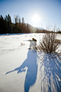 Hunter in snow camouflage takes aim on a sunny winter day