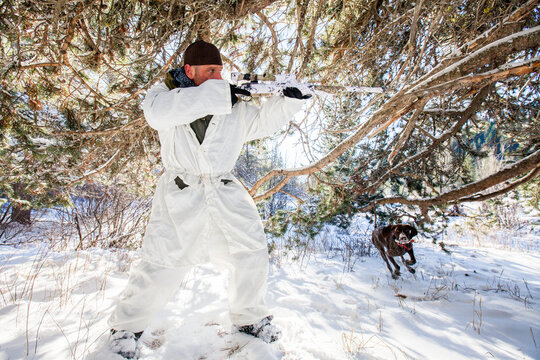 A hunter wearing  a coldweather camouflage outfit aims his rifel in