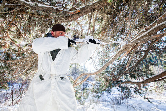 Man in white camouflage aims a rifle in a snowy forest
