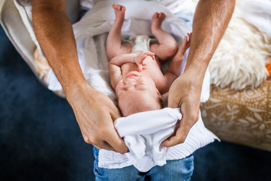A father dresses his newborn in a white onesie