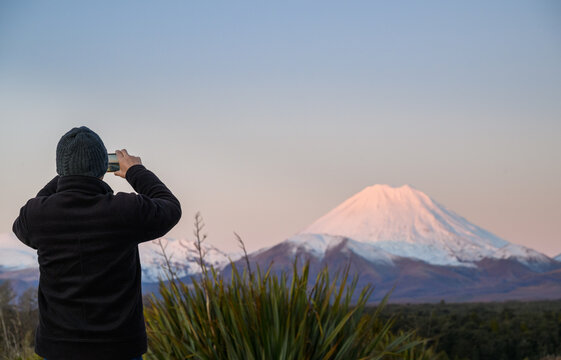 Tourist taking smartphone photos of Mt Ngauruhoe at sunset. Tongariro National Park. New Zealand.