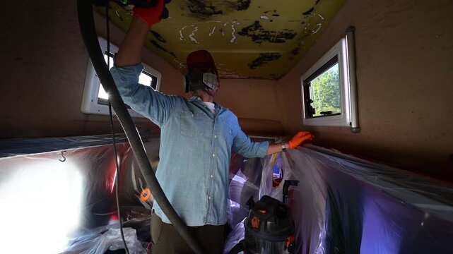 Man with protective gear sanding the ceiling of a camper van