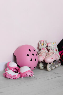 Pink kids roller skates, helmet, protective gear, and sports bag set against a light wall. Rollerblading and active kid leisure concept