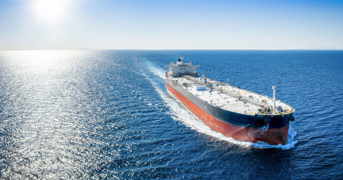 Aerial view of a crude oil super tanker ship traveling with speed over the sparkling ocean as a transport concept for fossil fuel