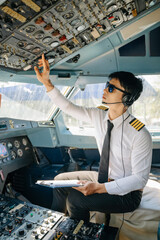 A focused airline pilot wearing a headset checks instrument gauges on the cockpit dashboard with a clipboard during preflight. © Nuttapong punna