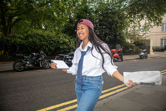 Smiling hipster woman walks on London street holding a newspaper