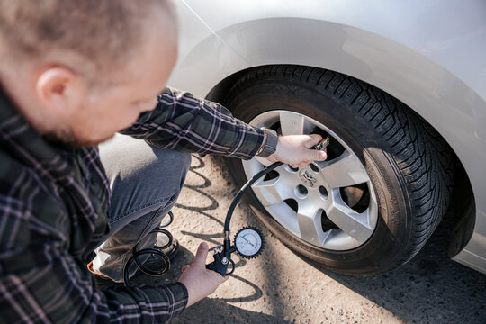 Driver kneeling and checking car tire pressure with air pump