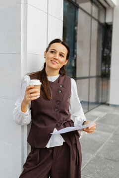 Smiling businesswoman holding coffee and document outdoors
