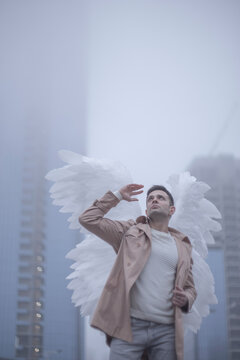 Man with angel wings looking up in foggy city skyline with copy space