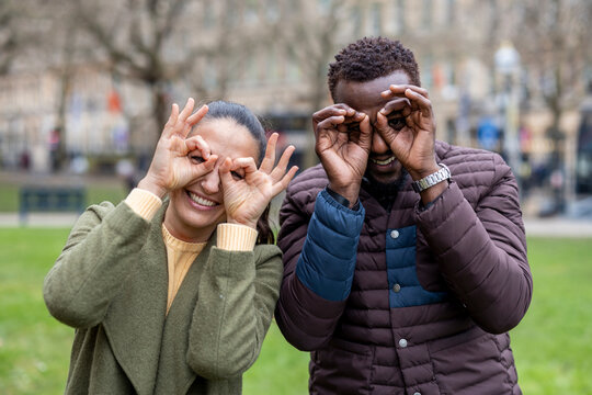 Playful couple making glasses gesture with hands in city park