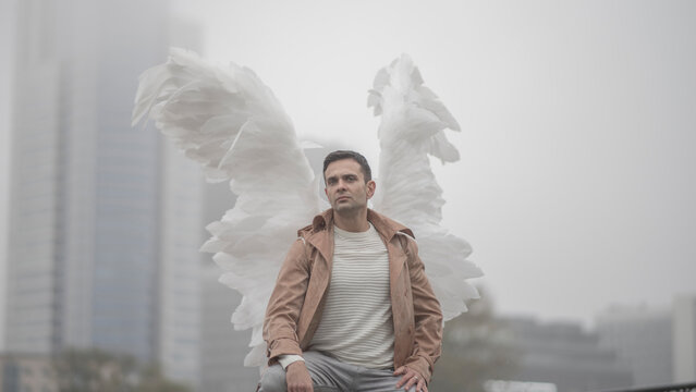 Confident man with angel wings standing in foggy metropolis with copy space