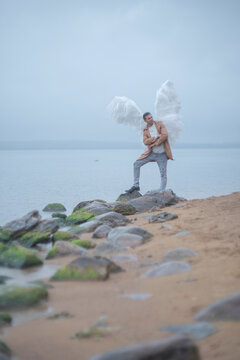 Proud man with white angel wings standing on rocks by misty shore with copy space