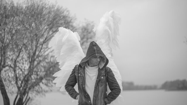 Depressed man with white angel wings wearing denim jacket hood with copy space