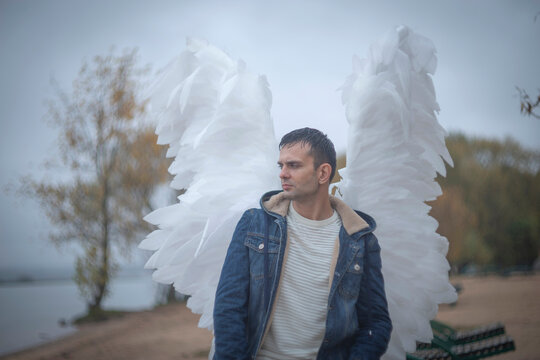 Thoughtful man with large white angel wings on autumn lakeside beach with copy space