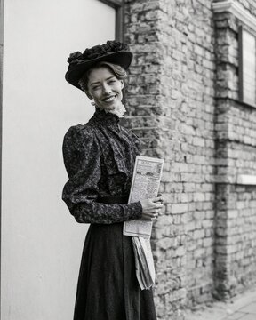 1900s suffragette holding a pamphlet beside a large blank brick building facade