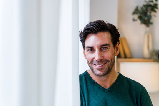 Man smiling indoors beside white curtain in modern living space