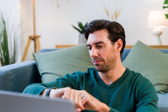 White man checking wristwatch while sitting on couch in living room