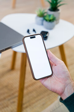 Smartphone held above white table with laptop and wireless earbuds