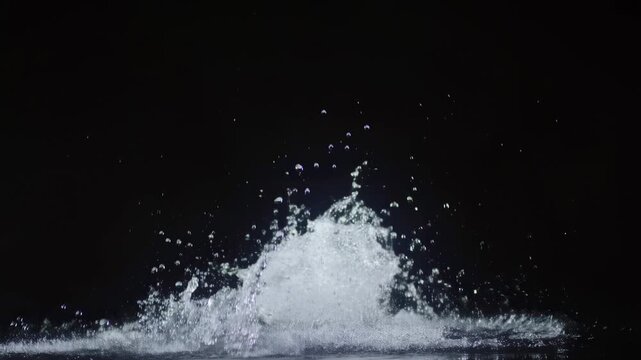 Water splash erupts from a dark surface with droplets scattering against a black studio background. Beverage advertising, hydration campaigns, and liquid product promotion.