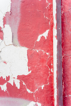 Peeling and cracked red and white paint texture on weathered wall