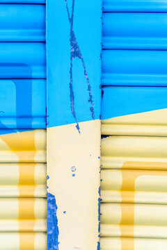 Weathered metal shutter with peeling blue and yellow paint