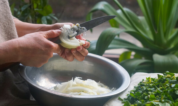 Slicing white onion into a bowl for green somsa preparation.