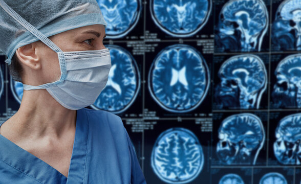 Female neurosurgeon in medical mask and cap looking at brain MRI scans background. Diagnostics of cerebral tumors and stroke.