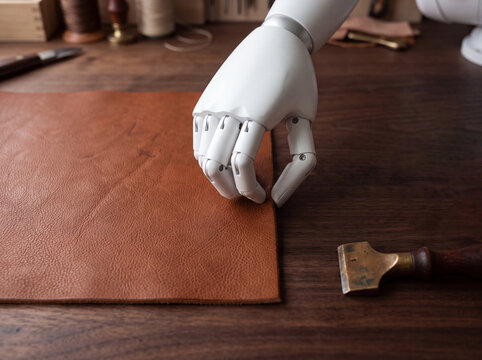 Futuristic robotic hand examining brown genuine leather next to human hand in a traditional craft workshop