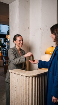 Friendly female hotel receptionist giving a room key to a guest at the boutique reception desk