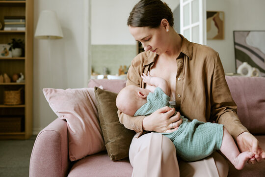 Caucasian young adult mother breastfeeding infant baby indoors, representing maternal care, postpartum health, natural lactation support, family wellness, maternity lifestyle campaigns