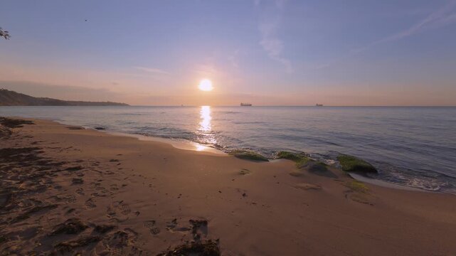 Golden sunrise video over calm sea with cargo ships on horizon and sandy beach