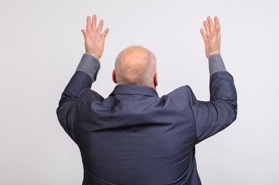 Back view of bald man in suit raising hands up on gray background