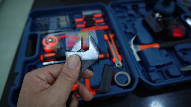 Hand technician in work holding an adjustable wrench. Adjusting the adjustable wrench. Video. Macro close-up hand man holds an adjustable wrench and opens it, with a tool case in the background.