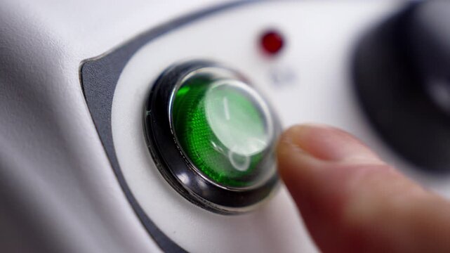 Close up of finger pressing illuminated green power switch button on a white electronic device control panel to turn off appliance