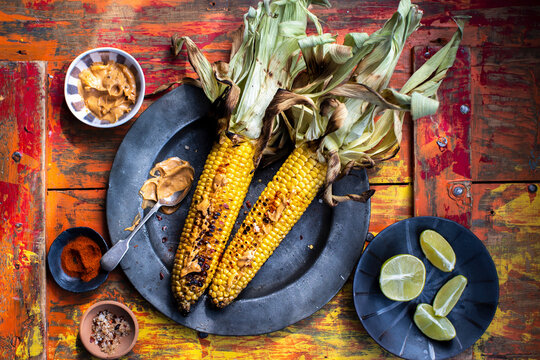 Grilled corn on the cob with mustard sauce, spices, and lime wedges