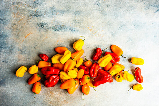Fresh mixed yellow, red, and orange chili peppers on gray background