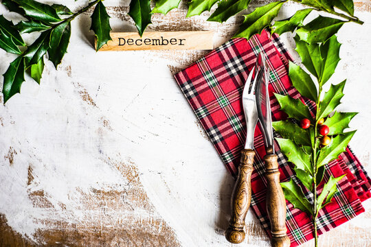 Vintage cutlery setting on red plaid napkin with holly decoration