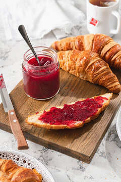 Red gooseberry jam spread on Croissant slice with Croissants and tea