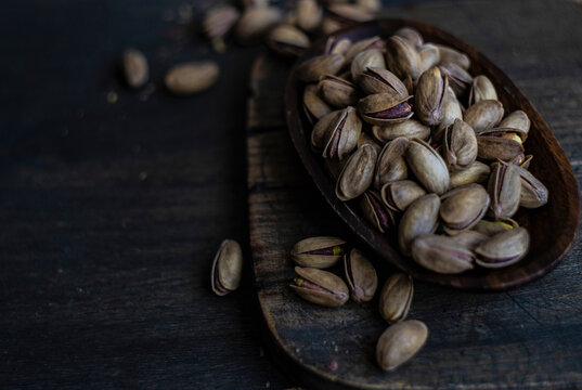 Pistachios in wooden bowl on dark wooden surface