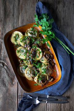 Round ravioli with mushroom sauce and herbs on rustic wood