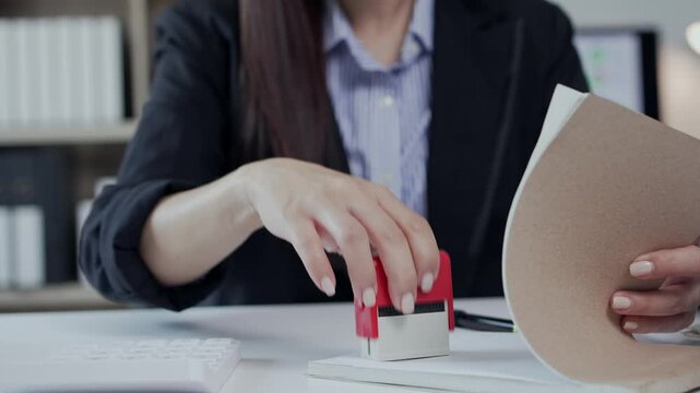 Businesswoman stamping official documents with an approved stamp for contract validation in the office