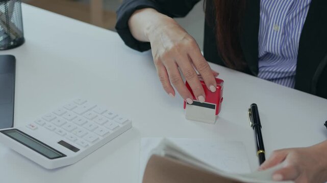 Businesswoman stamping documents with an approved seal on an office desk for authorization and agreement